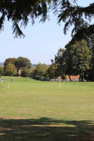 Churcher's School outdoor grass courts on a sunny day, with rugby posts and sports field markings surrounded by trees.