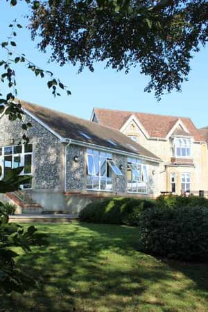 Outdoor view of Churcher's School student dormitories with traditional stone and brick architecture surrounded by greenery.