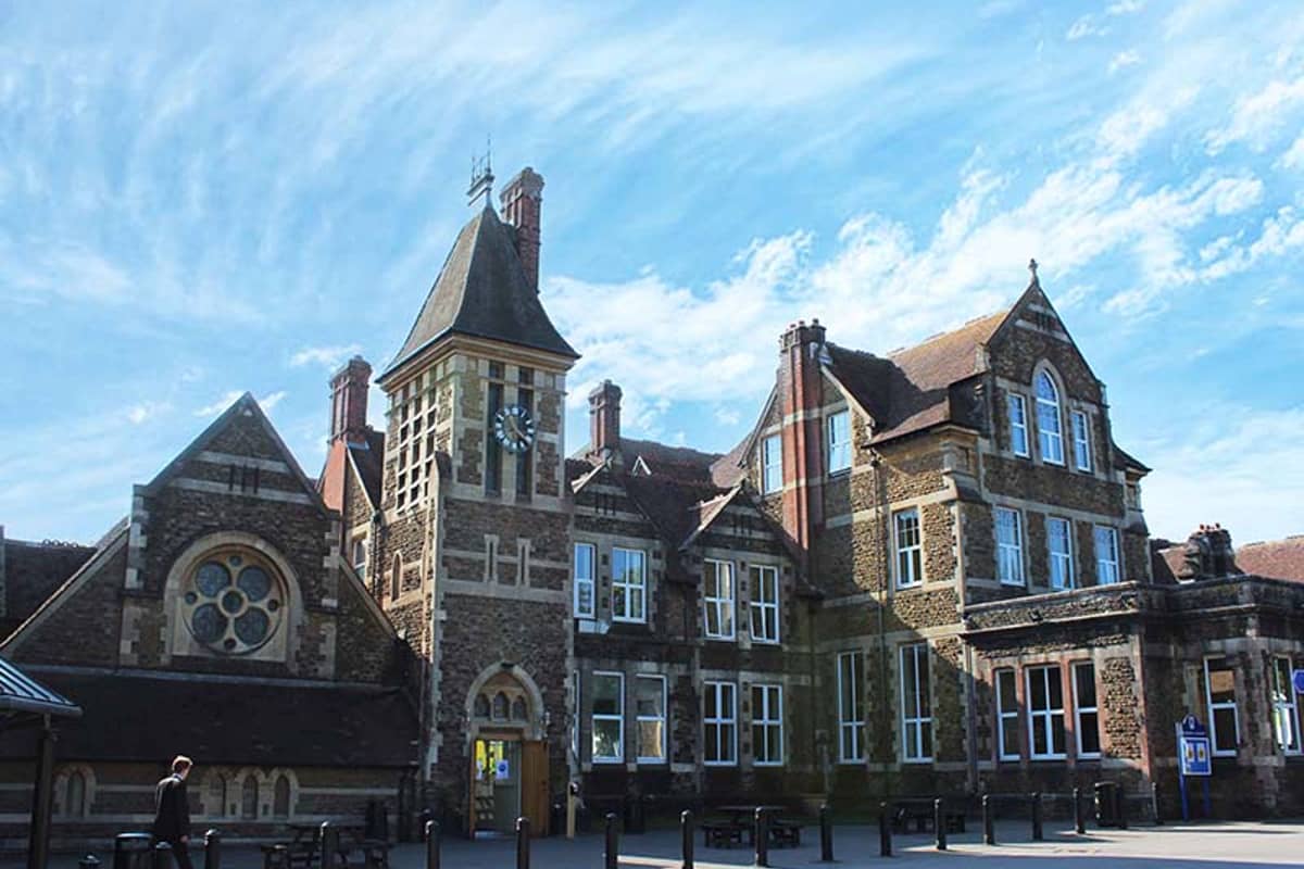 Wide shot of Churcher's College exterior, featuring a clock tower, arched windows, and decorative brickwork under a blue sky.