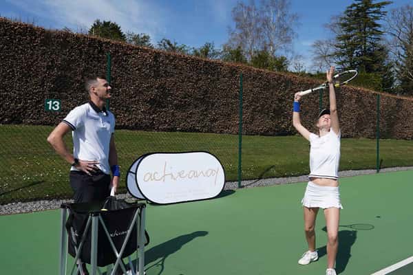 Jamie Murray coaching a student on a grass tennis court at Churcher's College, with the student poised to hit the ball.