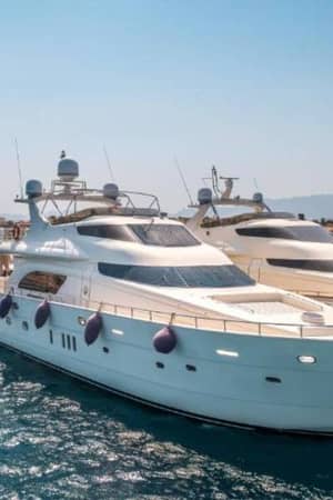 Two white motor yachts docked at a marina, showcasing sleek designs and luxurious features, with a clear sky and distant mountains in the background.