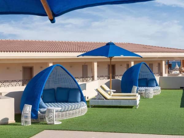 Outdoor lounge with canopy sofas and blue umbrellas on faux grass at Cleopatra Gallery.