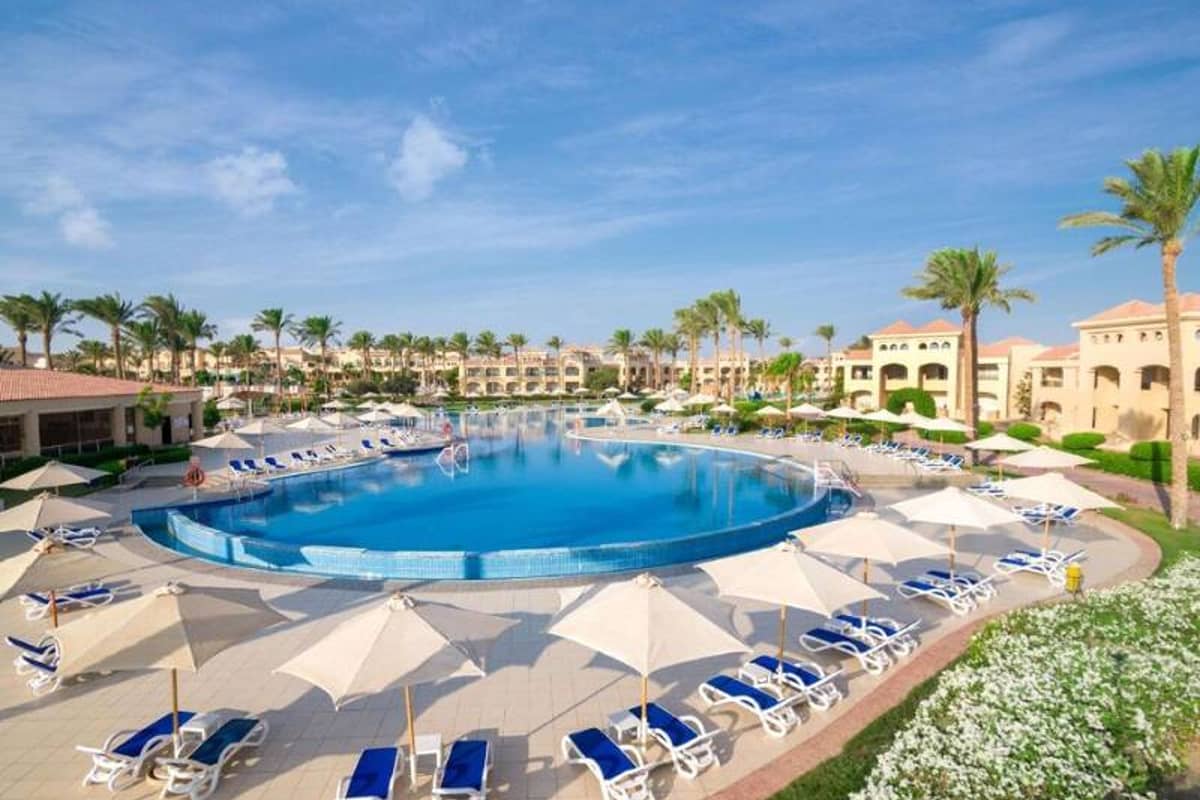 Aerial view of Cleopatra Luxury Resort's circular swimming pool, with loungers and umbrellas, surrounded by lush gardens.