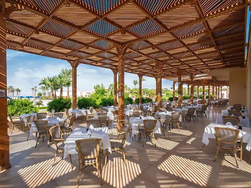 Alfresco dining area at Cleopatra Luxury Resort with wooden pergolas, set tables, greenery, and palm trees in the background.