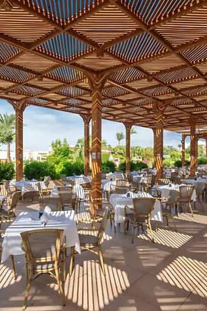 Alfresco dining area at Cleopatra Luxury Resort with wooden pergolas, set tables, greenery, and palm trees in the background.
