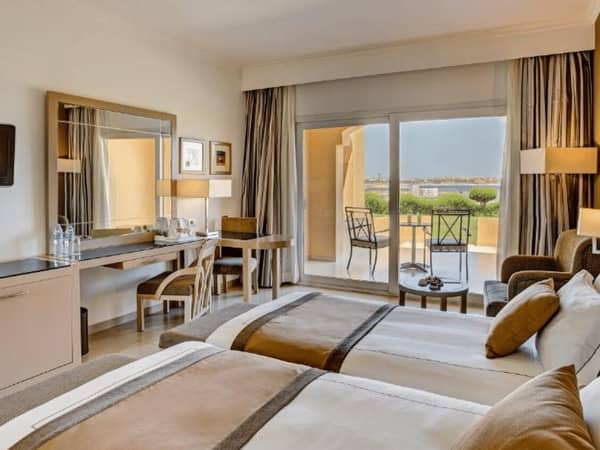 Deluxe room with twin beds in Cleopatra Luxury Resort, featuring a desk, seating area, and balcony with beach view.