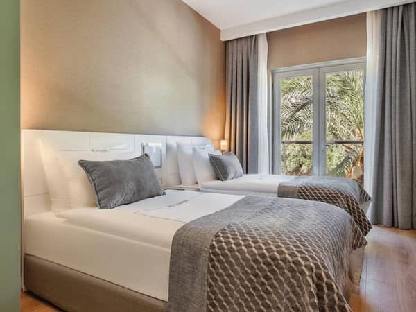 Corendon family room with two double beds, elegant bedding, modern decor, and a view of greenery through a large window.