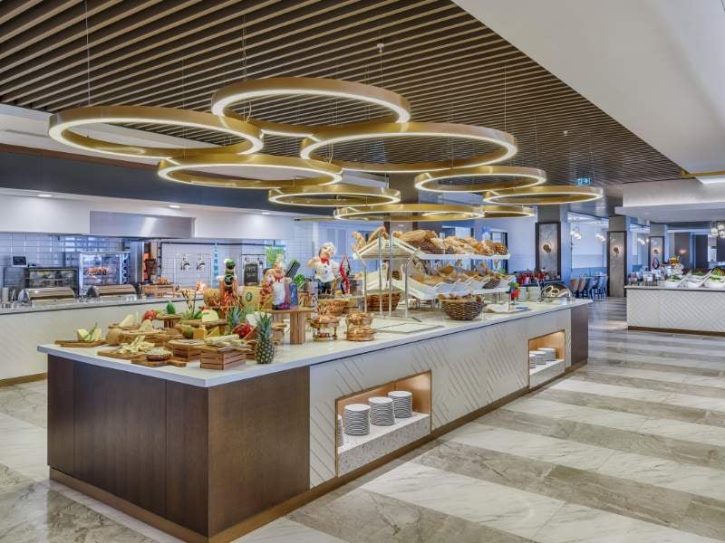 Buffet area in a modern dining space with various food items, stylish lighting, and a contemporary design at Corendon.