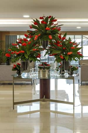 Luxurious hotel lobby with red flowers on a glass table, grey sofas, and large windows.