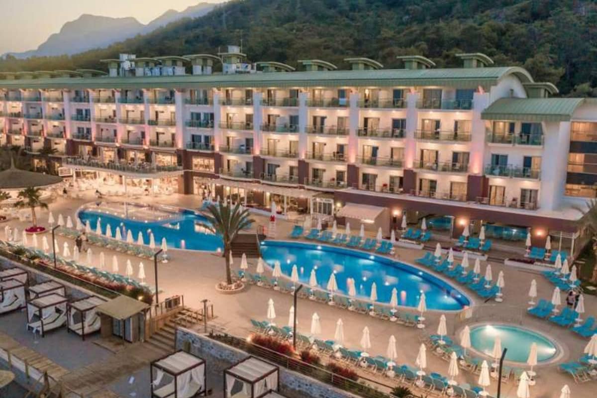 Aerial view of Corendon resort with a large swimming pool, sun loungers, umbrellas, and a hotel building set against green hills.