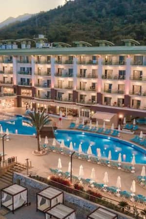 Aerial view of Corendon resort with a large swimming pool, sun loungers, umbrellas, and a hotel building set against green hills.