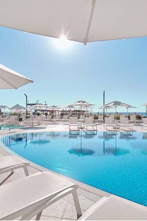Relaxing poolside scene at Corendon Playa Kemer, featuring sun loungers, umbrellas, and a view of the sea under a clear blue sky.