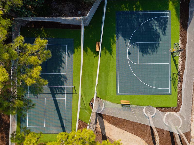 Aerial view of tennis and basketball courts at Corendon Playa Kemer, surrounded by green artificial turf and benches.