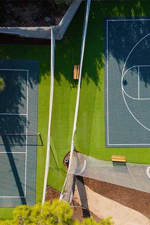 Aerial view of tennis and basketball courts at Corendon Playa Kemer, surrounded by green artificial turf and benches.