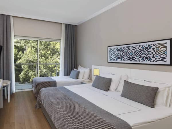 Hotel room with two double beds, grey and white bedding, a large window revealing greenery, and a decorative artwork above the beds.