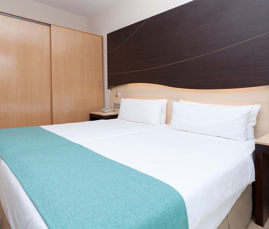 Hotel room at Impressive Playa Granada Golf with a double bed, white linens, teal runner, and a dark wooden headboard with lighting.