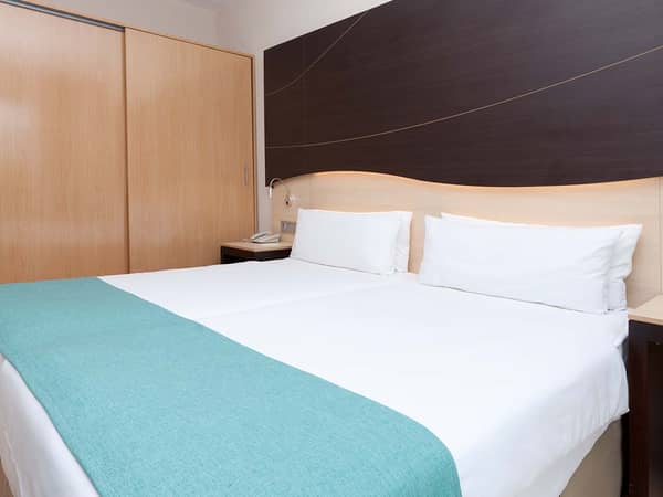 Hotel room at Impressive Playa Granada Golf with a double bed, white linens, teal runner, and a dark wooden headboard with lighting.