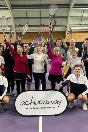 Group of tennis players at DL Bristol Gallery holding up racquets, participating in an Active Away event on an indoor court.