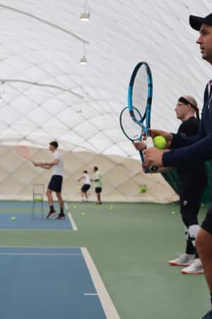Tennis players and a coach at an indoor court during an Active Away session in Beaconsfield, poised to play.