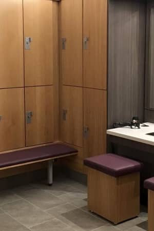 Modern changing room at DL-Beaconsfield with wooden lockers, upholstered seating, and a vanity area with mirrors and basins.