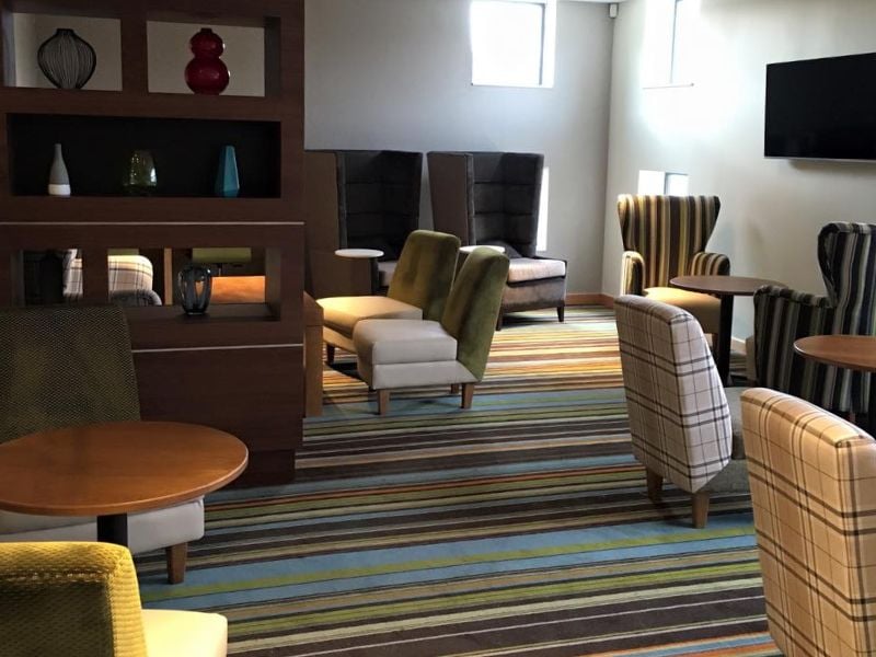 Modern club room with assorted armchairs, sofas, decorative shelving with vases, a flat-screen television, and striped carpet.