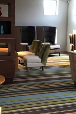 Modern club room with assorted armchairs, sofas, decorative shelving with vases, a flat-screen television, and striped carpet.