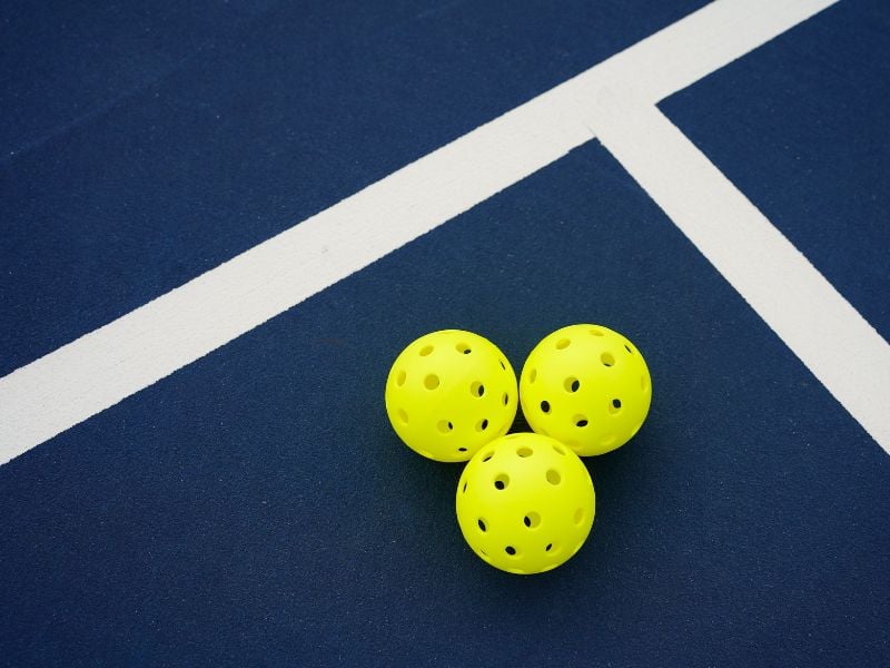 Three yellow pickleballs on a dark blue court with intersecting white lines.