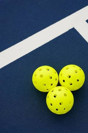 Three yellow pickleballs on a dark blue court with intersecting white lines.