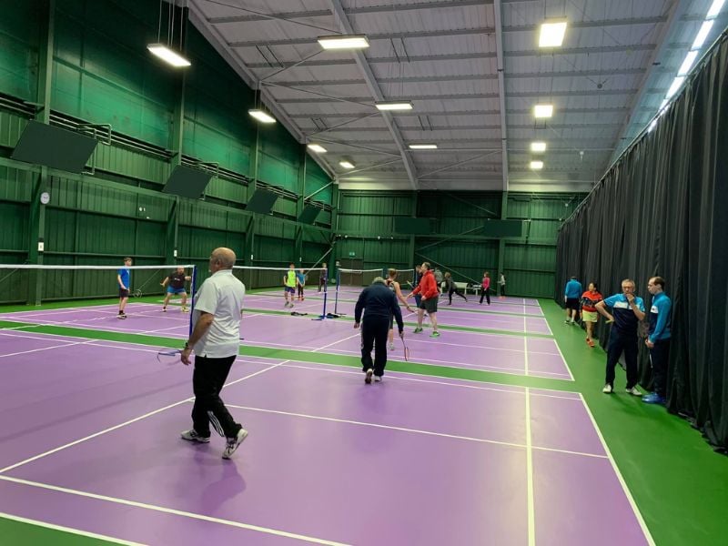 Multiple games of pickleball in progress at DL Bristol's indoor courts, with players of various ages on purple courts surrounded by green walls.