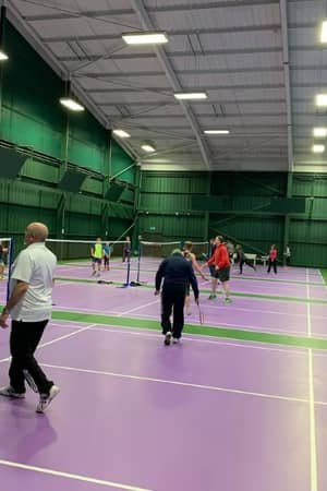 Multiple games of pickleball in progress at DL Bristol's indoor courts, with players of various ages on purple courts surrounded by green walls.