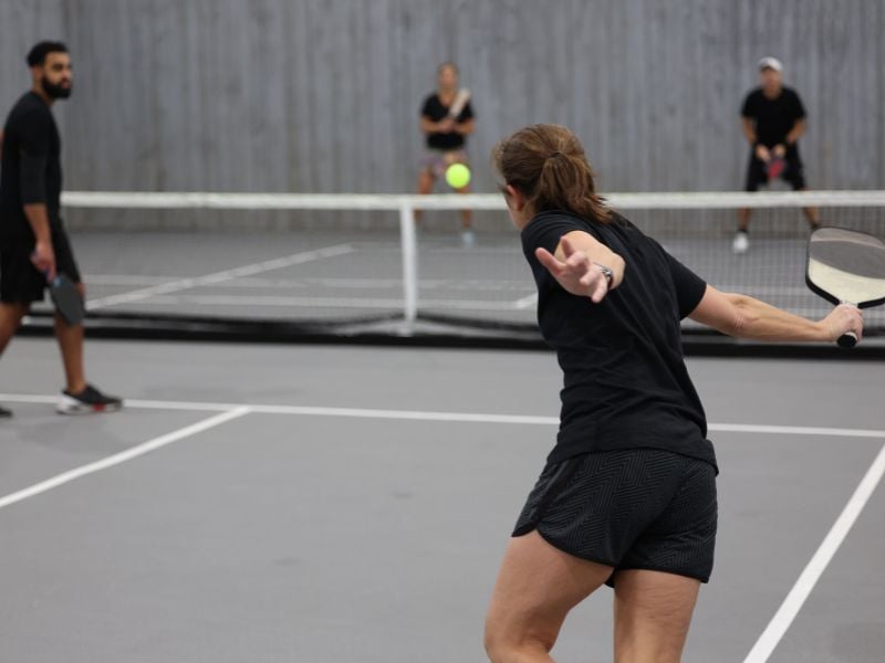 Four players engaging in a pickleball game on an indoor court, with one player poised to return the ball.