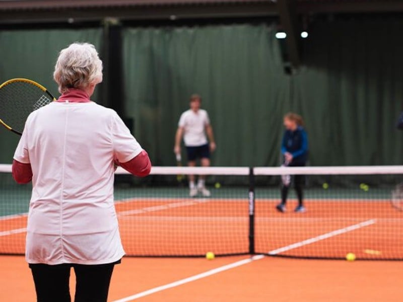 Indoor tennis lesson at DL Cheshire Oaks with a coach observing a young player on court.