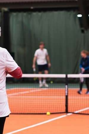 Indoor tennis lesson at DL Cheshire Oaks with a coach observing a young player on court.