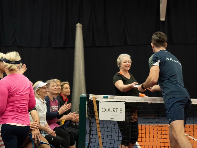 Tennis coach distributing refreshments to female players on a bench at Cheshire Oaks.
