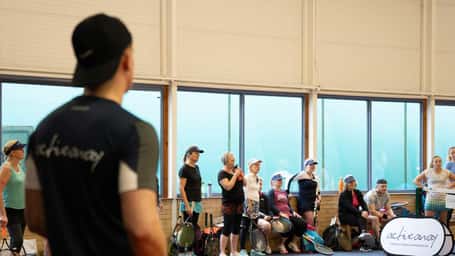 Tennis players listening to an instructor during a training session at DL Cheshire Oaks indoor facility.