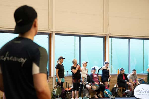 Tennis players listening to an instructor during a training session at DL Cheshire Oaks indoor facility.