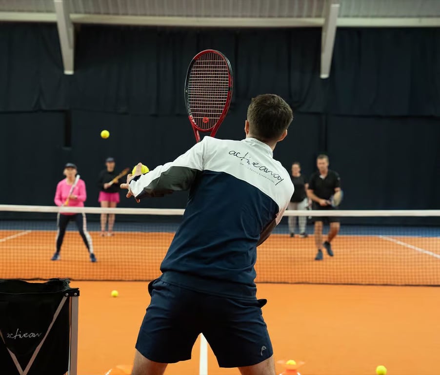 Tennis coach serving on indoor court with players ready for training, showcasing dynamic sports practice.