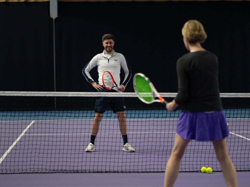 Tennis coach instructing a student during a practice session at DL Chorley Gallery indoor court.