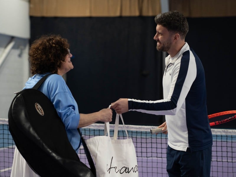 Man and woman on an indoor tennis court at DL Chorley Gallery, engaging in a friendly exchange with tennis gear in hand.