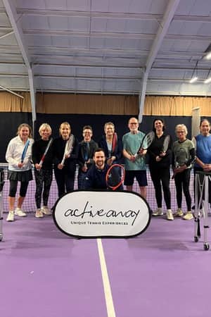 Group photo of participants at the Active Away tennis break in Edinburgh, standing on a purple indoor court holding tennis rackets and a banner.