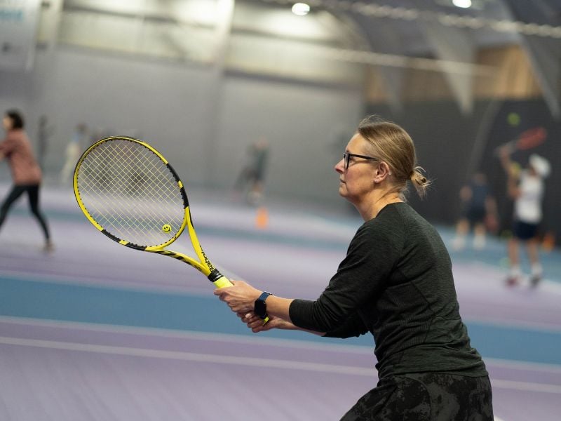 Female tennis player holding a yellow racket, preparing to return a shot at DL Edinburgh's indoor tennis court.