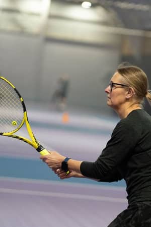 Female tennis player holding a yellow racket, preparing to return a shot at DL Edinburgh's indoor tennis court.