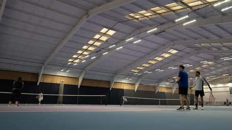 Indoor tennis court at DL Finchley with players in a doubles match, under a high ceiling.