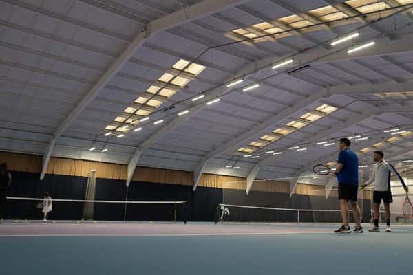 Indoor tennis court at DL Finchley with players in a doubles match, under a high ceiling.