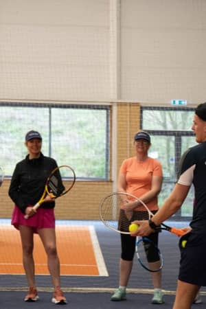 Tennis group coaching session at DL Hull with coach Alex instructing five players holding rackets on an indoor court.