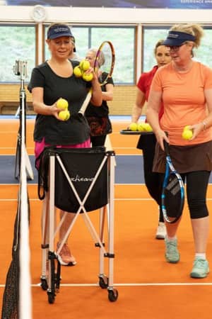 Tennis players at DL Hull Gallery preparing for drills, holding rackets and balls on a vibrant orange and blue court.