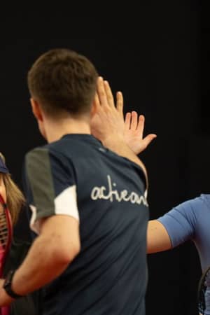 Tennis players sharing a high five at DL Hull Gallery, with a smiling onlooker nearby.