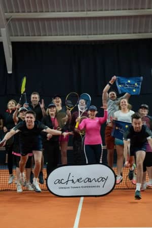 A group of excited tennis players jumping with rackets on an indoor court, promoting Active Away's unique tennis experiences.