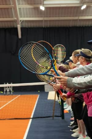 Group of people during a tennis coaching session with instructor Josh at DL MK Gallery, all holding racquets and standing on an indoor court.