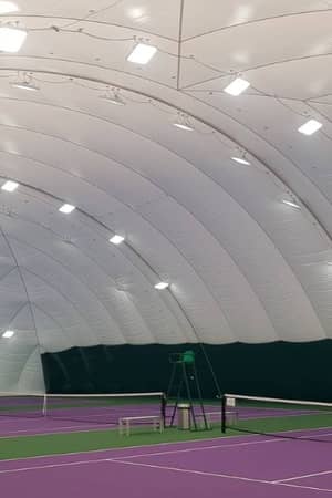 Indoor tennis court in an inflatable dome with a purple surface, lighting fixtures on the ceiling, and green boundary lines.